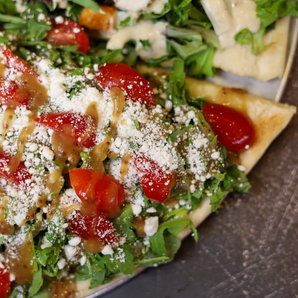 Close-up of a Sorella's Pizza & Pasta pizza slice topped with arugula, tomatoes, cheese, and dressing.