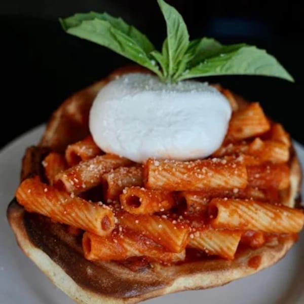 Rigatoni pasta with red sauce, parmesan, and a large dollop of burrata cheese, garnished with basil.