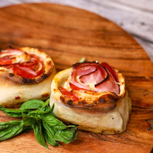 Two Sorella's Pizza & Pasta ham and cheese rolls with basil on a wooden board.